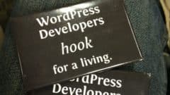 Two black sticker badges reading "WordPress Developers hook for a living" on a gray fabric surface.