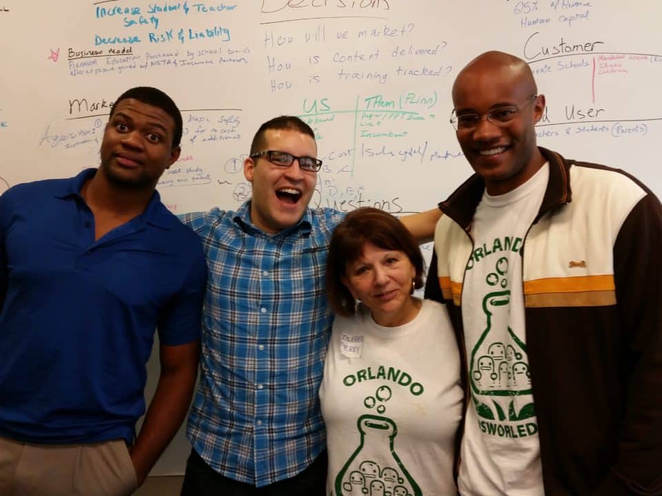 Four team members smiling in front of a whiteboard filled with business strategy notes and diagrams.