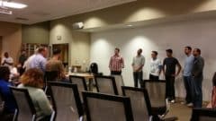 Group of people standing and sitting in a conference room during what appears to be a team meeting or workshop presentation.