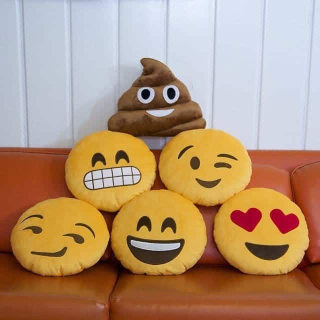 Colorful emoji plush pillows arranged on an orange couch displaying various happy facial expressions.