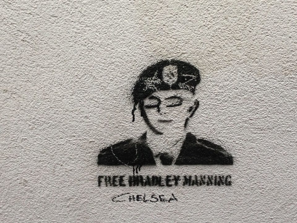 Stencil street art portrait supporting Bradley Manning with Chelsea name reference on textured wall.