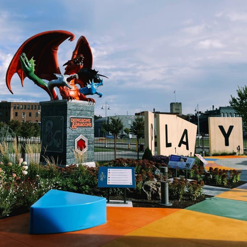 Statues in the Strong Museum of Play Hasbro statue garden. The statues are of Scrabble tiles spelling the word "PLAY", Trivial Pursuit pieces, and a large Tiamat from Dungeons and Dragons