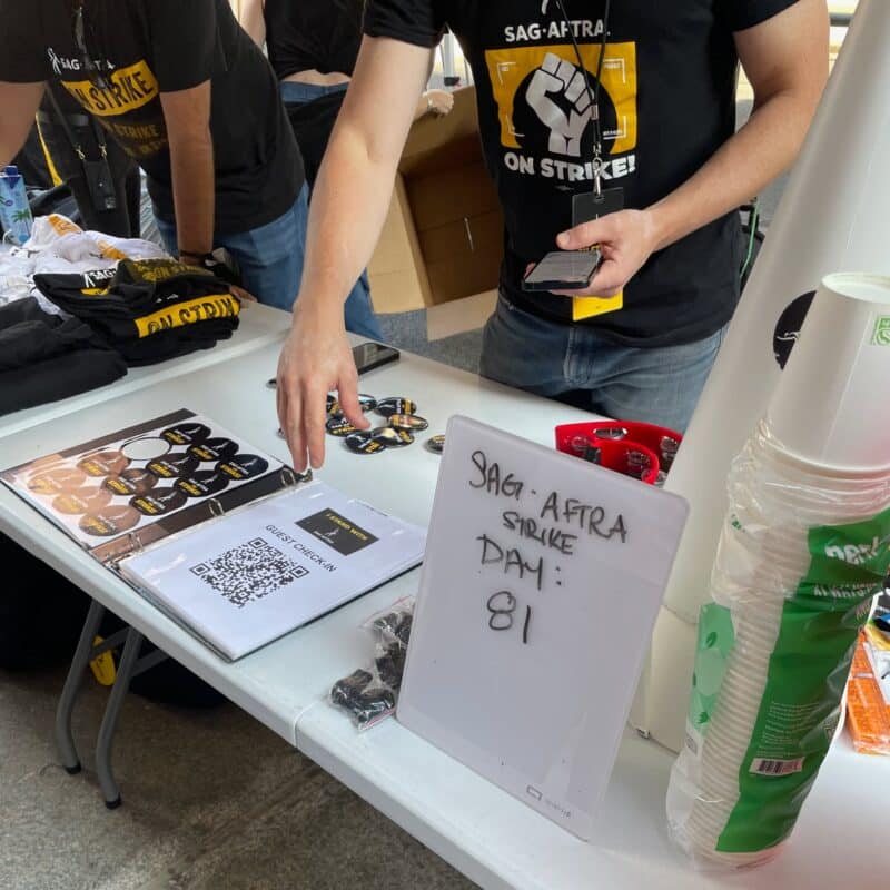 A volunteer passing out stickers and pins, as well as showing guest check-in at a table for the SAG-AFTRA strike Day 81