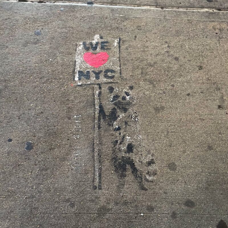 street art of a raccoon holding up a sign that says We Heart NYC
