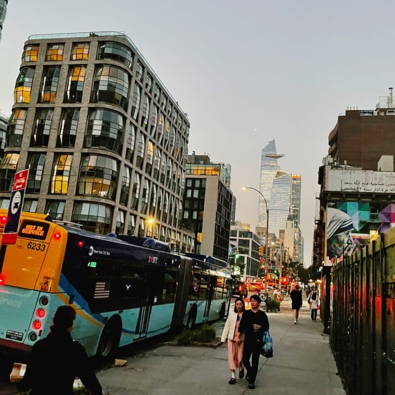 the street in NYC showing some buildings, a bus, and some people walking