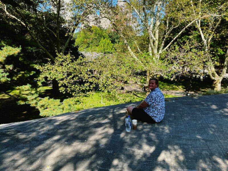 Timothy sitting on a large rock, looking toward the camera in Central Park in NYC