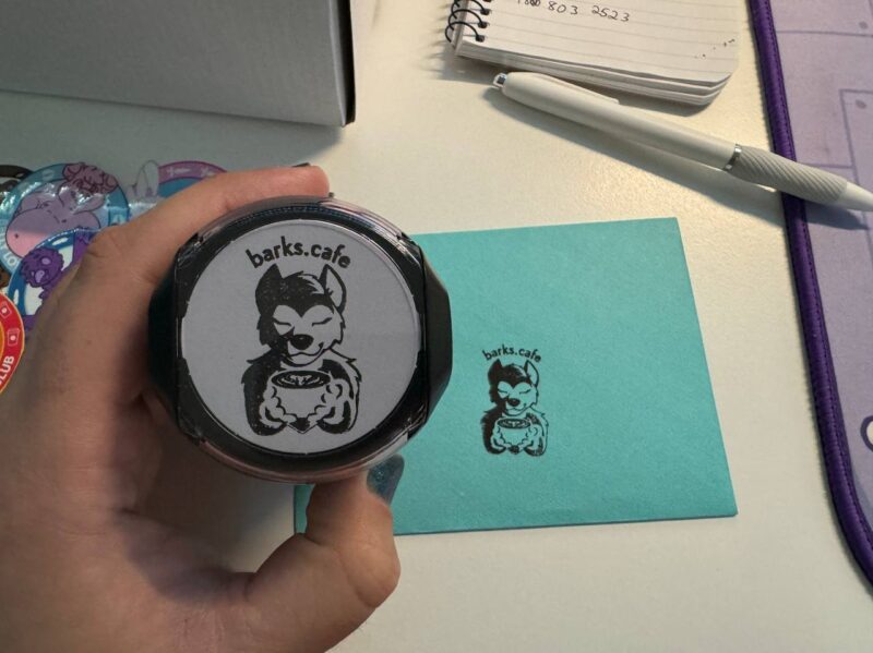 A stamp of a dog holding a latte with the text barks.cafe above the head. This is in front of an envelope with the stamp on it