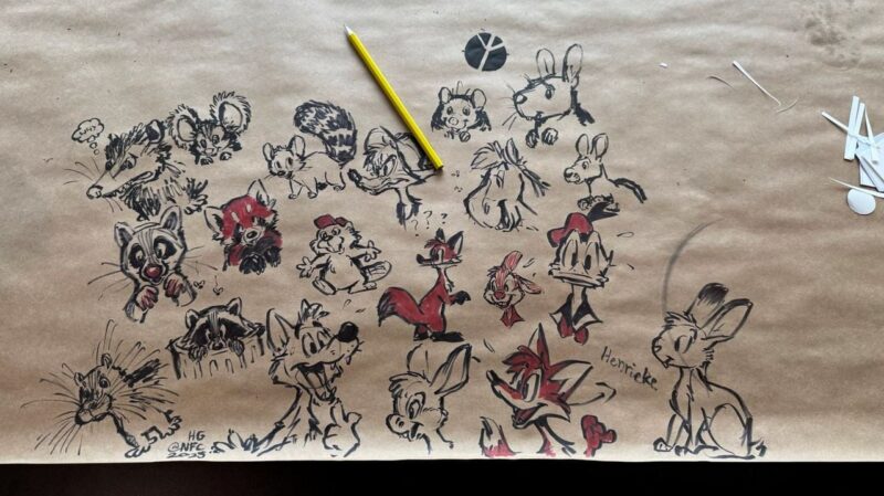 A large sheet of brown paper features a collection of animal sketches drawn in black and red ink. The illustrations include various cartoon-like characters such as foxes, rabbits, and raccoons, some with exaggerated expressions. A yellow pencil lies on the paper, suggesting ongoing work. The name Henrieke is written near one of the drawings.