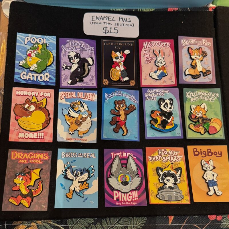 A display of fifteen colorful enamel pins featuring various cartoon animals with humorous themes. Each pin is mounted on a rectangular card with playful slogans, such as “Pool Gator,” “Hungry for More,” “Birds Are Real,” and “Dragons Are Cool.” The animals include an alligator, skunk, fortune cat, rabbit, dragon,