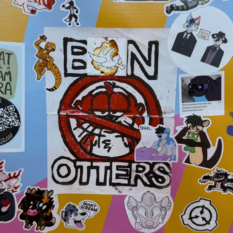 The image shows a colorful collection of various stickers on a background with different shades. In the center, a prominent sticker displays BAN OTTERS with a red crossed-out sign over a cartoon otter face. Surrounding it are multiple other stickers depicting cartoon characters, including animals and anthropomorphic figures, some dressed in suits. Different styles and themes are
