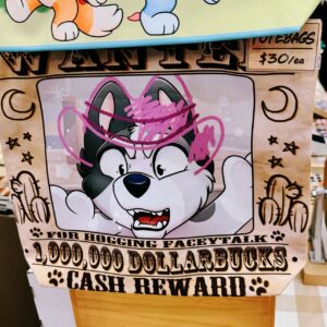 A humorous graphic on a tote bag designed as a Western-style wanted poster. It features a cartoon husky with a surprised expression, partly obscured by a pink cowboy hat drawn over its head. The poster humorously states, “Wanted for hogging faceytalk. 1,000,000 Dollarbucks cash reward.” Decorative elements include stars,