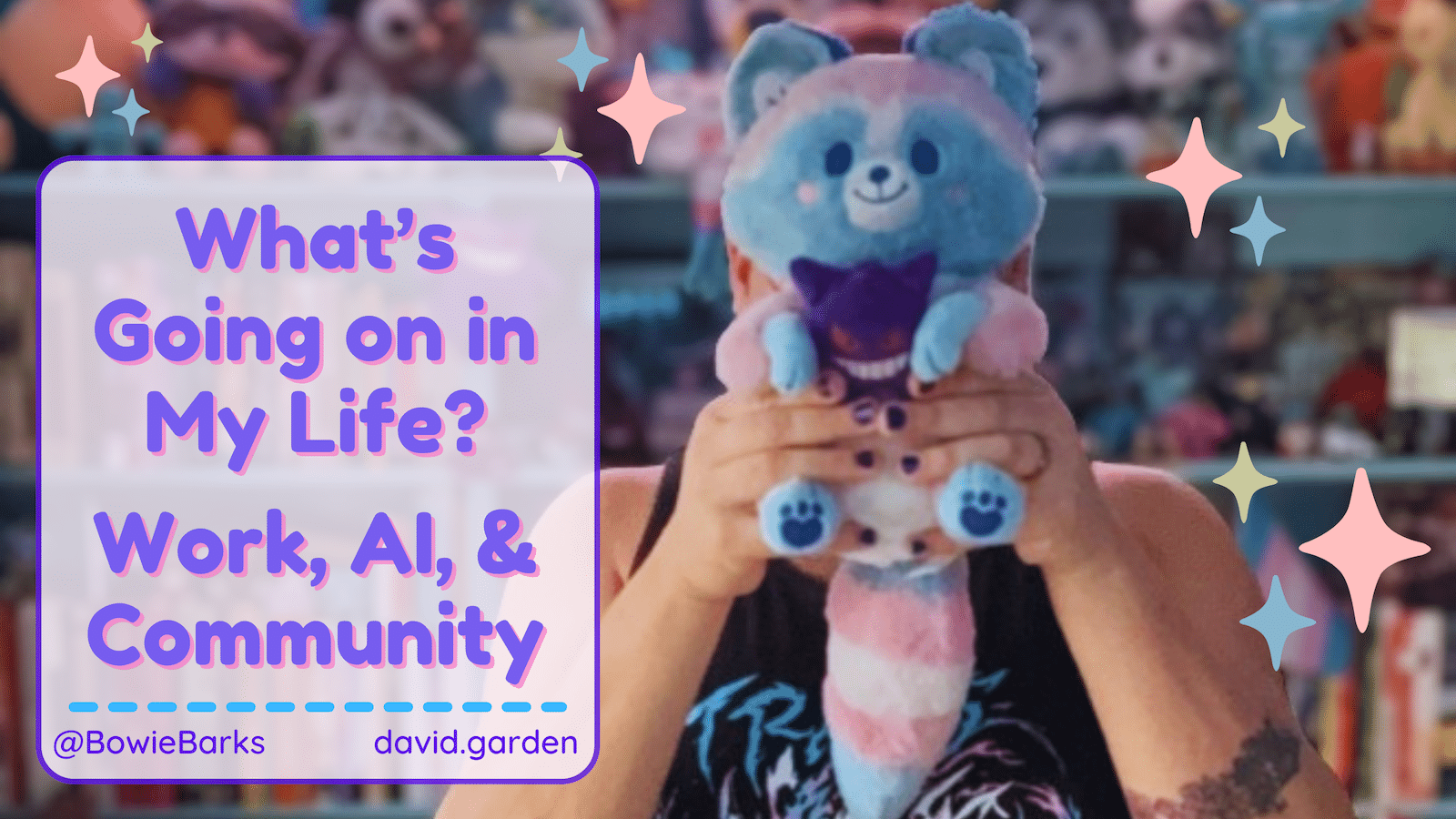 A person holding a cute, plush toy resembling a raccoon stands in front of a colorful backdrop filled with various other stuffed animals. The plush is pastel blue and pink with a purple bow. The text overlay reads, “What’s Going on in My Life? Work, AI, & Community.” The individual has short hair and is wearing a black sleeveless shirt adorned with a graphic design. The overall atmosphere is playful and vibrant, with sparkles and decorative elements enhancing the image.